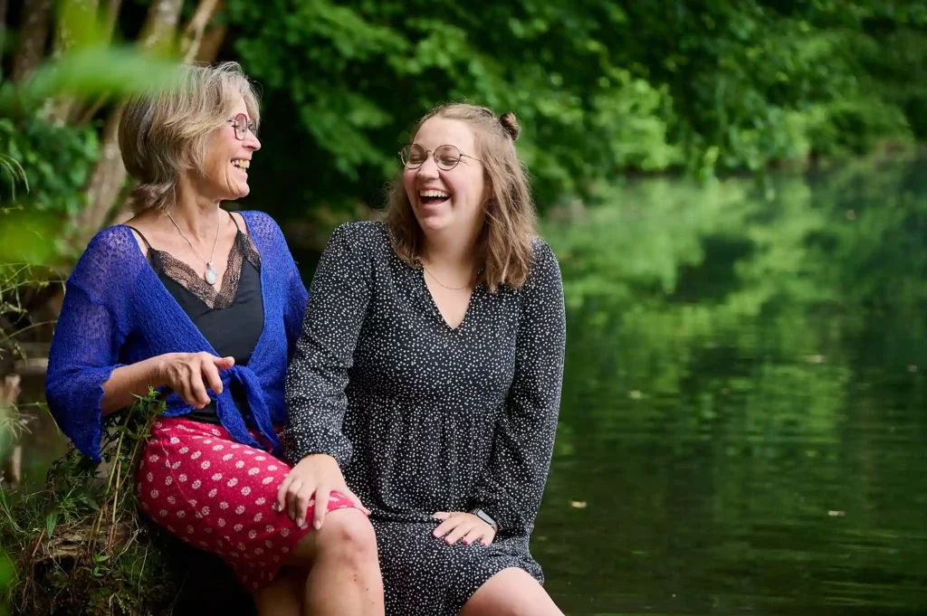 Mutter und Tochter lächeln und sitzen vor dem Fluss